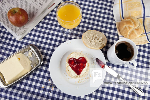 Ein Frühstückstisch mit einem Brötchen mit herzförmiger Marmelade darauf.