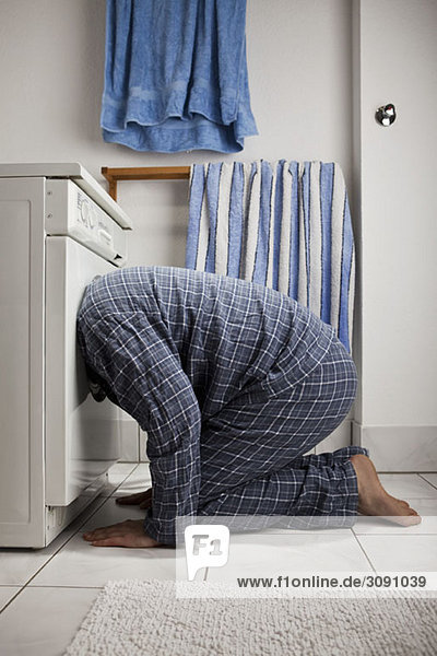 A man wearing pajamas with his head inside a washing machine