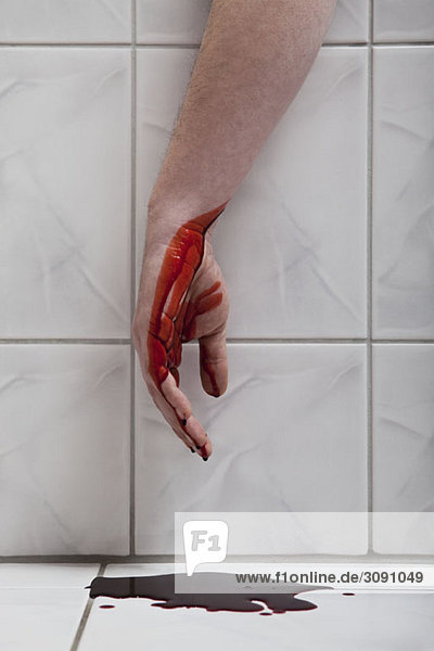 A human hand hanging from a bathtub with blood puddled beneath it