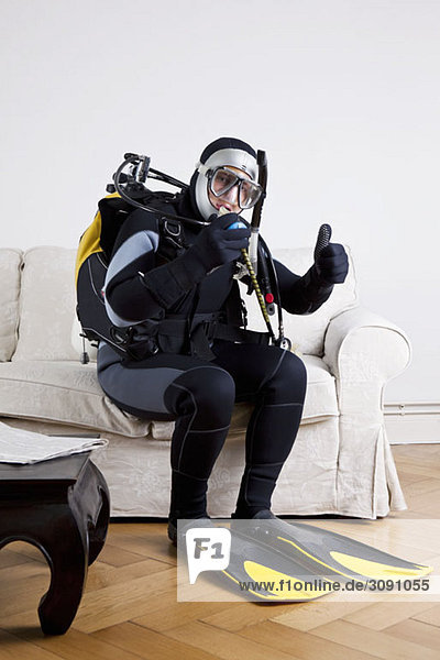 A scuba diver sitting on a couch in a living room giving a thumbs up sign