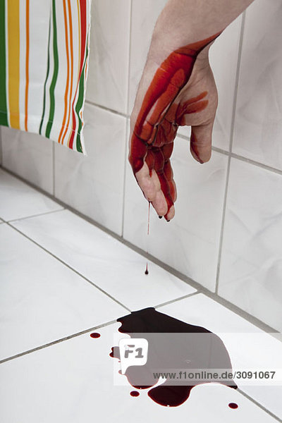 A human hand hanging from a bathtub with blood puddled beneath it