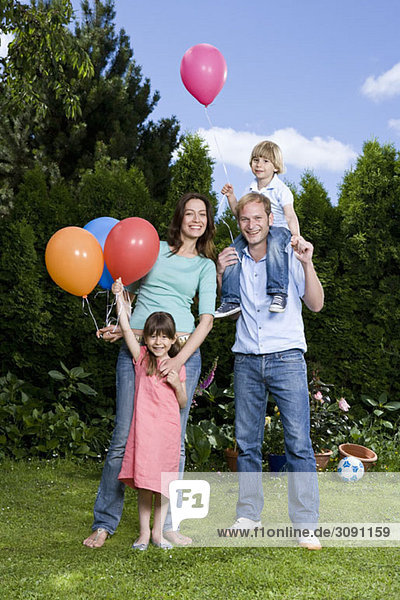 Zwei Eltern und ihre zwei Kinder halten Luftballons im Freien.