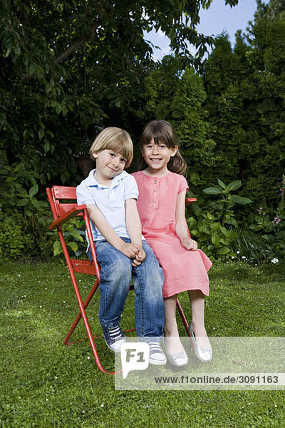 Ein junger Bruder und eine junge Schwester sitzen auf einem Stuhl im Freien.