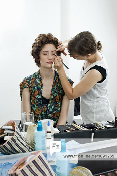 Ein Maskenbildner  der Make-up auf ein Modell aufträgt.