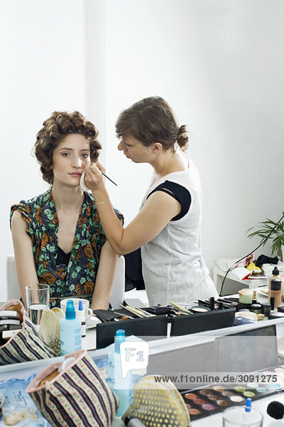 Ein Maskenbildner  der Make-up auf ein Modell aufträgt.