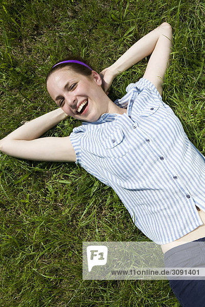 Eine junge Frau  die im Gras liegt und lacht.