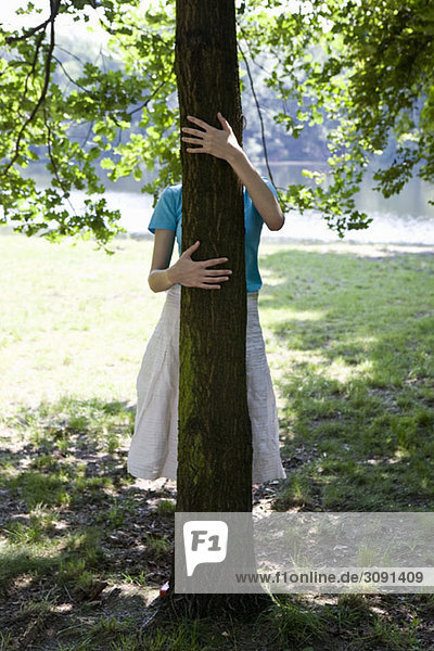 Eine junge Frau umarmt einen Baum  verdecktes Gesicht