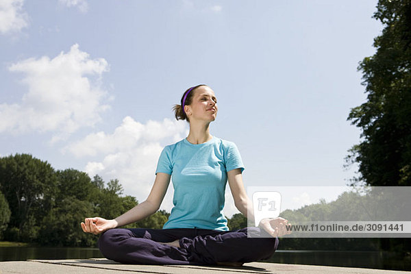 Eine junge Frau  die Yoga auf einem Steg praktiziert.