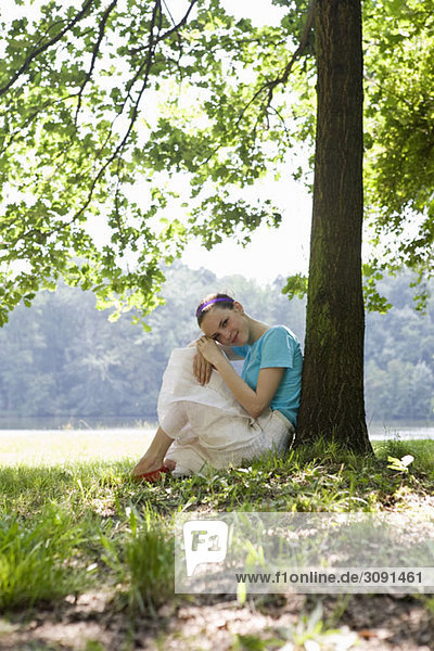 Eine junge Frau  die sich an einen Baum neben einem See lehnt.