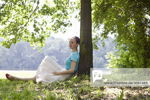 Eine junge Frau  die sich an einen Baum neben einem See lehnt.