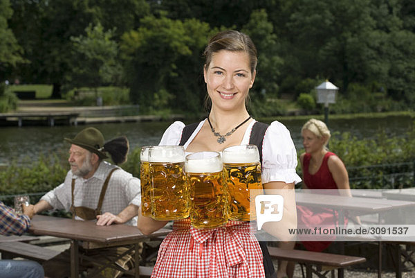 Eine traditionell gekleidete Deutsche serviert Bier im Biergarten