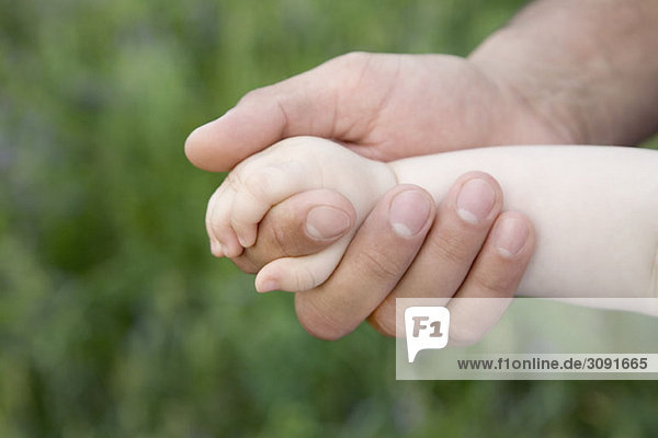 A baby holding the hand of an adult