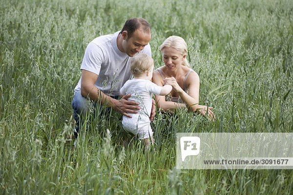 Zwei Eltern  die mit ihrer Tochter auf einem Feld spielen.