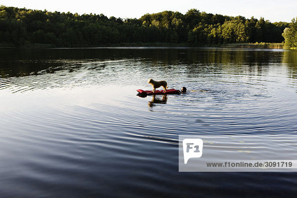 A man pushing a dog on a pool raft in a lake