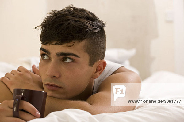 Ein junger Mann liegt im Bett und träumt mit einer Kaffeetasse.