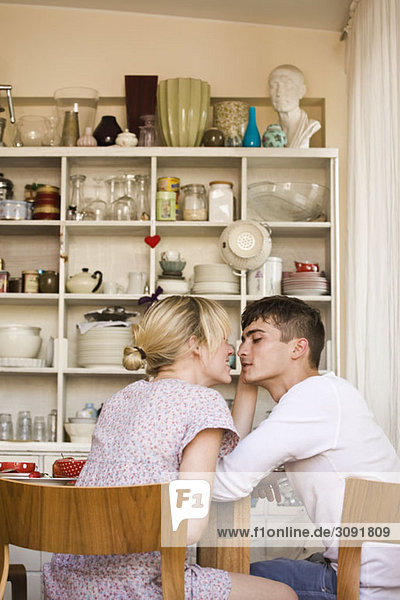 Ein junges  leidenschaftliches Paar  das in einer häuslichen Küche sitzt.