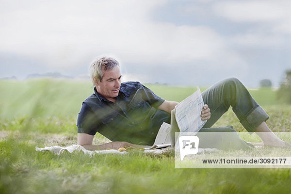 man sitting on grass reading newspaper