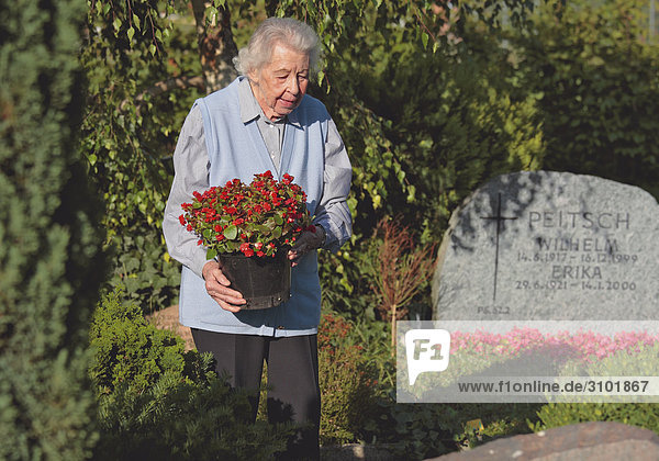 Seniorin bringt auf Friedhof Blumen an Grab