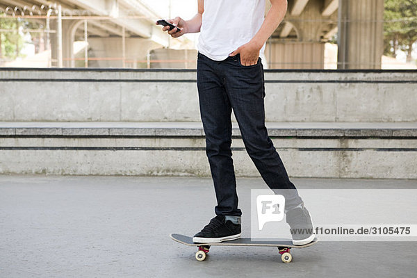 Teenager Junge auf Skateboard mit Handy