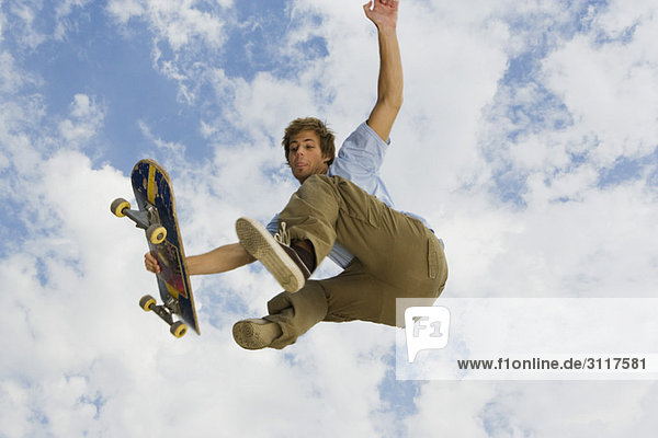 Junger Mann mit Skateboard-Trick in der Luft