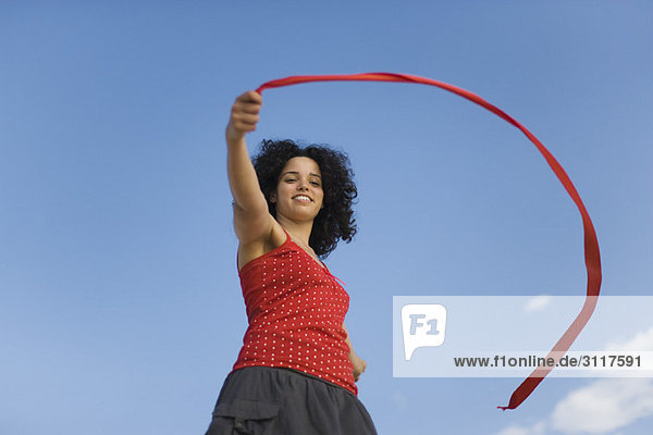 Junge Frau hält Band im Wind  lächelnd  flacher Blickwinkel