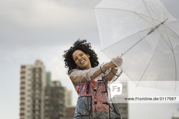 Junge Frau hält sich am windigen Tag am Regenschirm fest  lachend