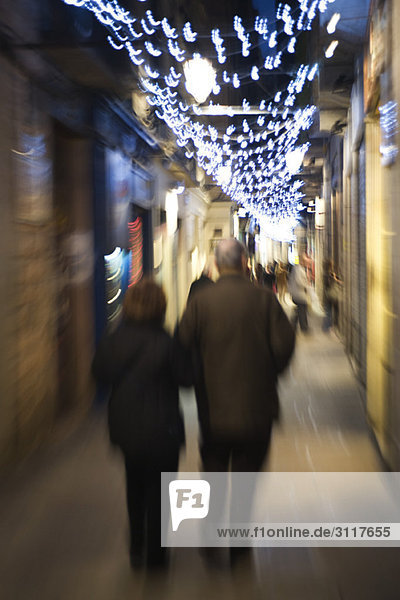 Couple walking down alley illuminated by Christmas lights at night
