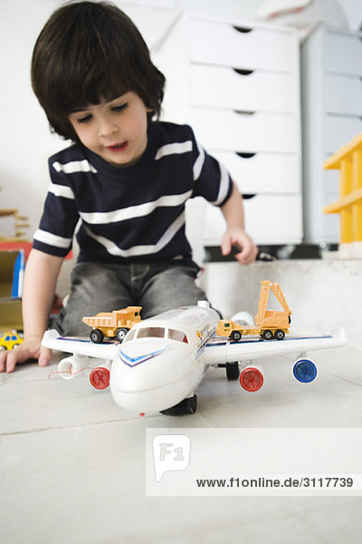 Kleiner Junge spielt mit Spielzeugflugzeug und Spielzeuglastwagen