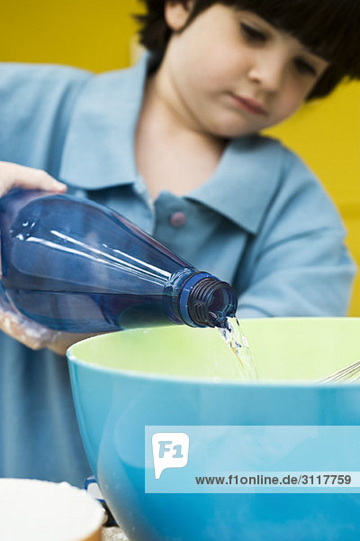 Kleiner Junge gießt abgefülltes Wasser in die Rührschüssel