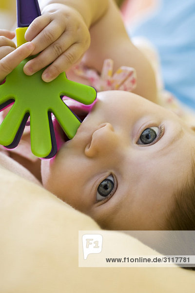 Kleinkind Mädchen kaut auf Plastikspielzeug  schaut in die Kamera