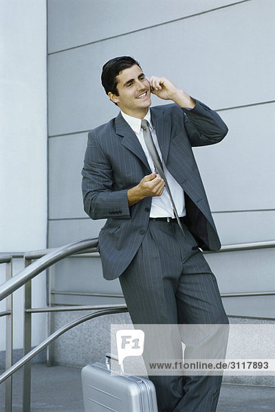 Businessman using cell phone  leaning against railing