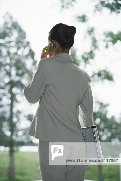Businesswoman using cell phone  carrying briefcase under arm  rear view
