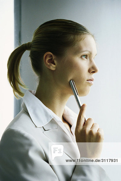 Young businesswoman looking away in thought  holding pen up to face