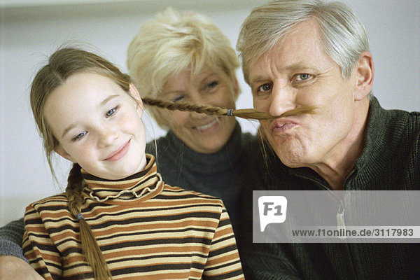 Young girl with grandparents  grandfather using girl's braid to imitate mustache