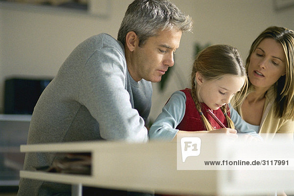 Eltern helfen der kleinen Tochter bei den Hausaufgaben