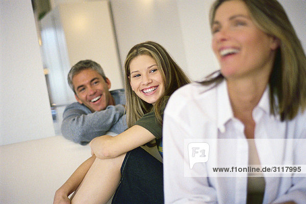 Teenagermädchen sitzend mit Eltern  alle lächelnd  Mutter lachend