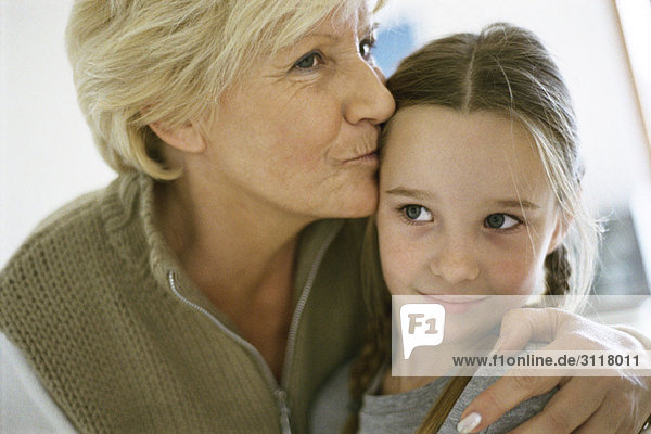 Senior woman with arm around granddaughter  kissing forehead  portrait