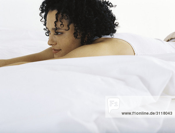 Frau auf dem Bett liegend  in Gedanken wegschauend