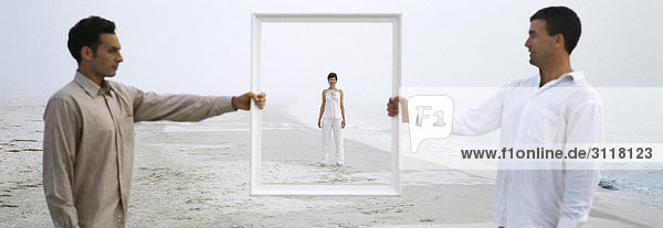 Woman on beach seen through picture frame held up by two men