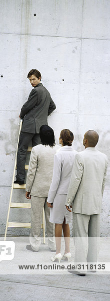 Businessman climbing ladder  looking over shoulder at professionals lined up behind him
