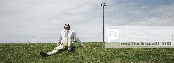 Businessman sitting in grass  leaning back enjoying sunny spell
