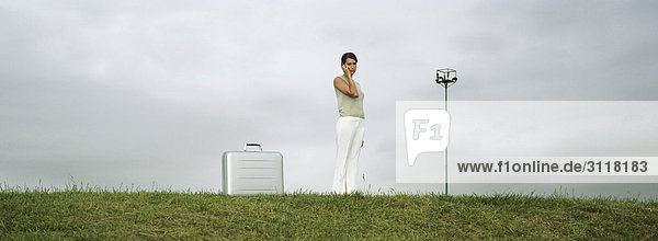 Frau im Feld stehend mit dem Handy  Aktentasche auf dem Boden in der Nähe