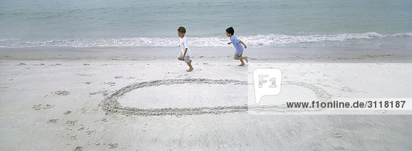 Boys running on beach  chasing each other around circle drawn in sand