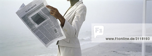 Frau in Geschäftskleidung liest Zeitung am Strand  abgeschnitten