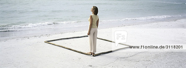 Frau steht in der Ecke des Platzes  der am Strand durch Längen von Bambus umrissen wird.
