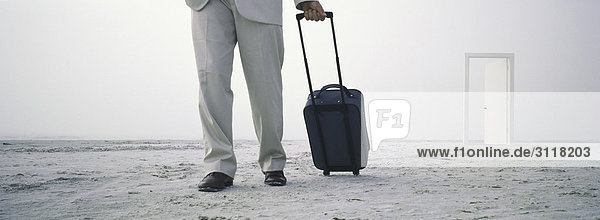 Man walking with rolling luggage on beach  open door in distance