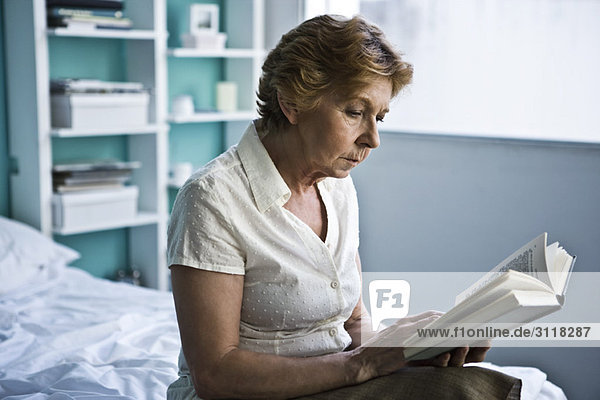Senior woman sitting on bed reading book