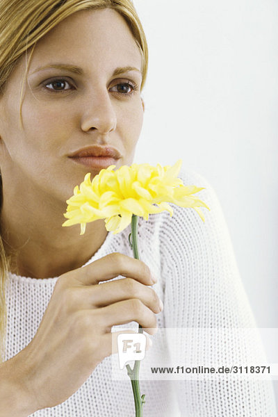 Frau hält Blume bis zur Nase,  nachdenklich wegschauend