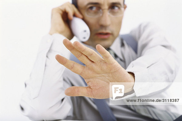 Geschäftsmann am Telefon der mit der Hand die Geste stoppt.