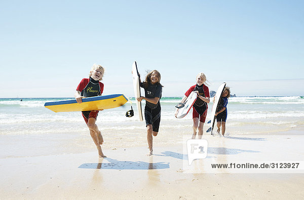 Kinder mit Surfbrettern rennen am Strand  Frontal